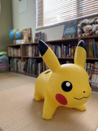 A large Pikachu doll standing in front of our children’s bookshelf.